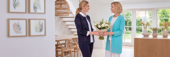 Twee vrouwen overhandigen elkaar glimlachend een boeket bloemen