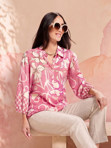 Zittende dame met zonnebril en een roze bloemenblouse met lange mouwen