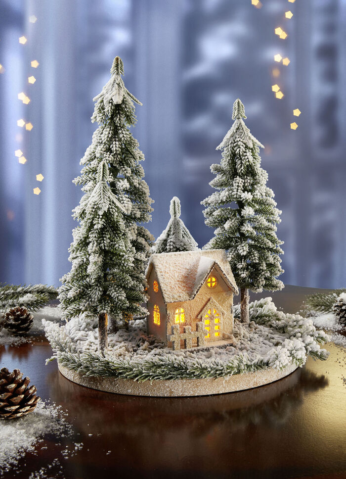Verlicht winterhuisje met dennenbomen 